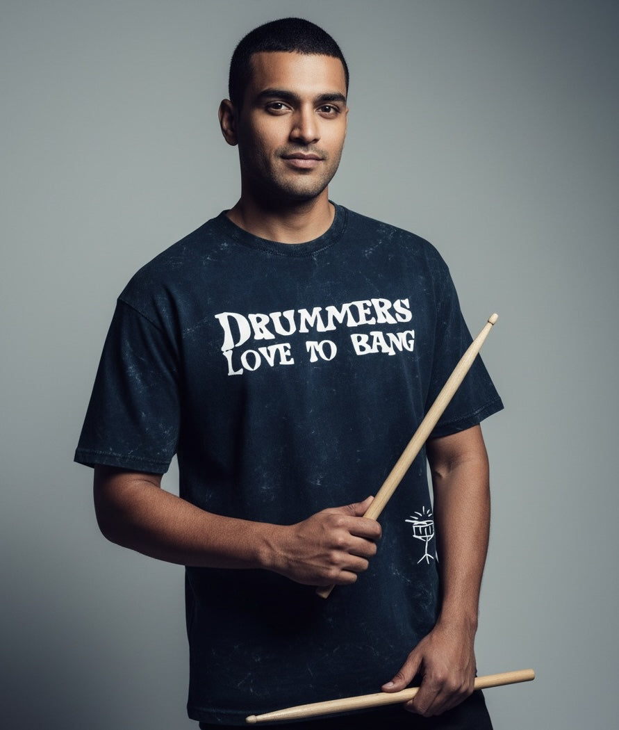 Man wearing a 'Drummers Love to Bang' t-shirt holding drumsticks against a gray background