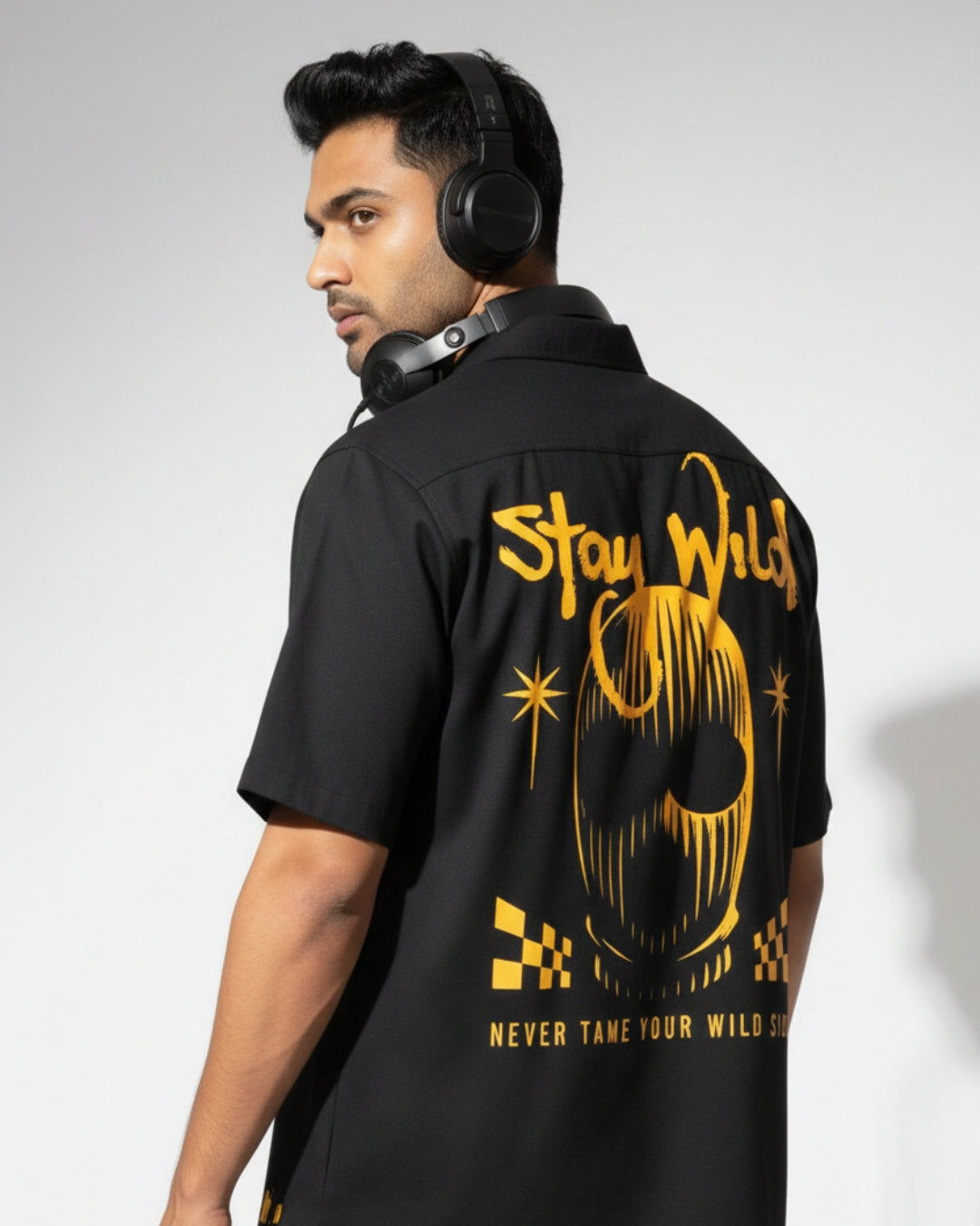 Man wearing a black shirt with yellow text and graphics on the back, standing against a plain background.