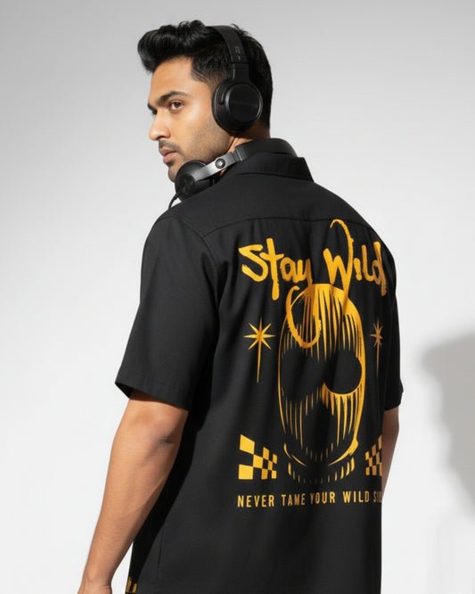 Man wearing a black shirt with yellow text and graphics on the back, standing against a plain background.