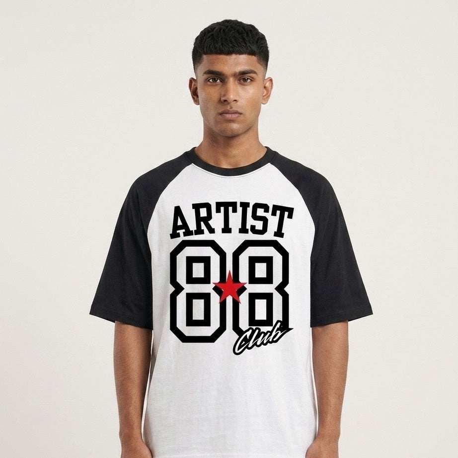 A man wearing a black and white raglan t-shirt with a graphic on the front that reads 'ARTIST 88 Club' in black and white with a small red star accent, set against a plain light background.