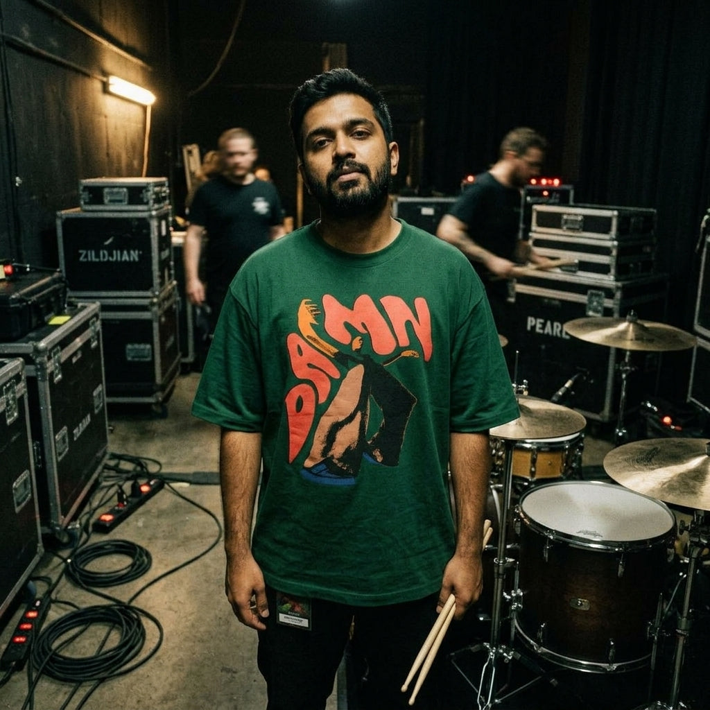 drummer in a green t-shirt with a DAMN graphic design standing in a music studio with drum equipment.