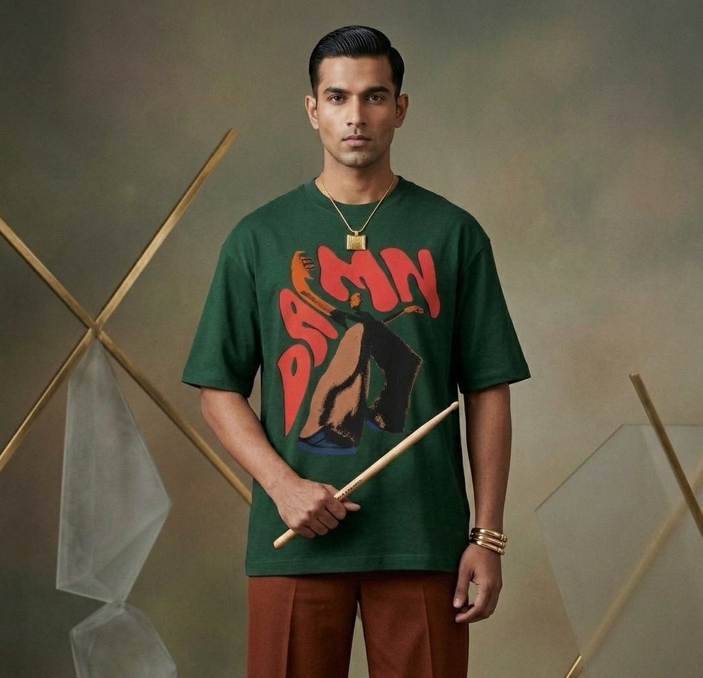 Man wearing a green t-shirt with DAMN graphic design, holding drumsticks against a neutral background