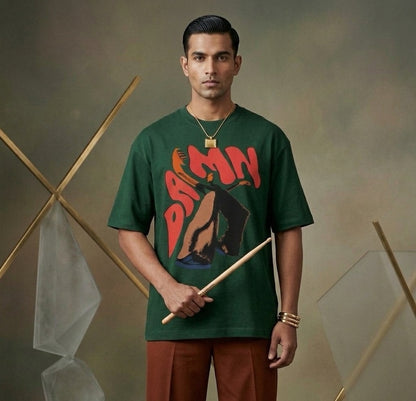 Man wearing a green t-shirt with DAMN graphic design, holding drumsticks against a neutral background