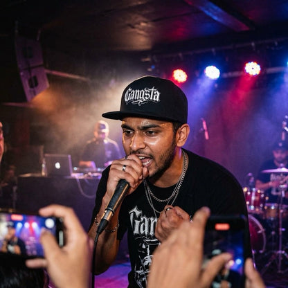 rapper singing into a microphone with 'Gangsta' cap at a concert with stage lights and audience.
