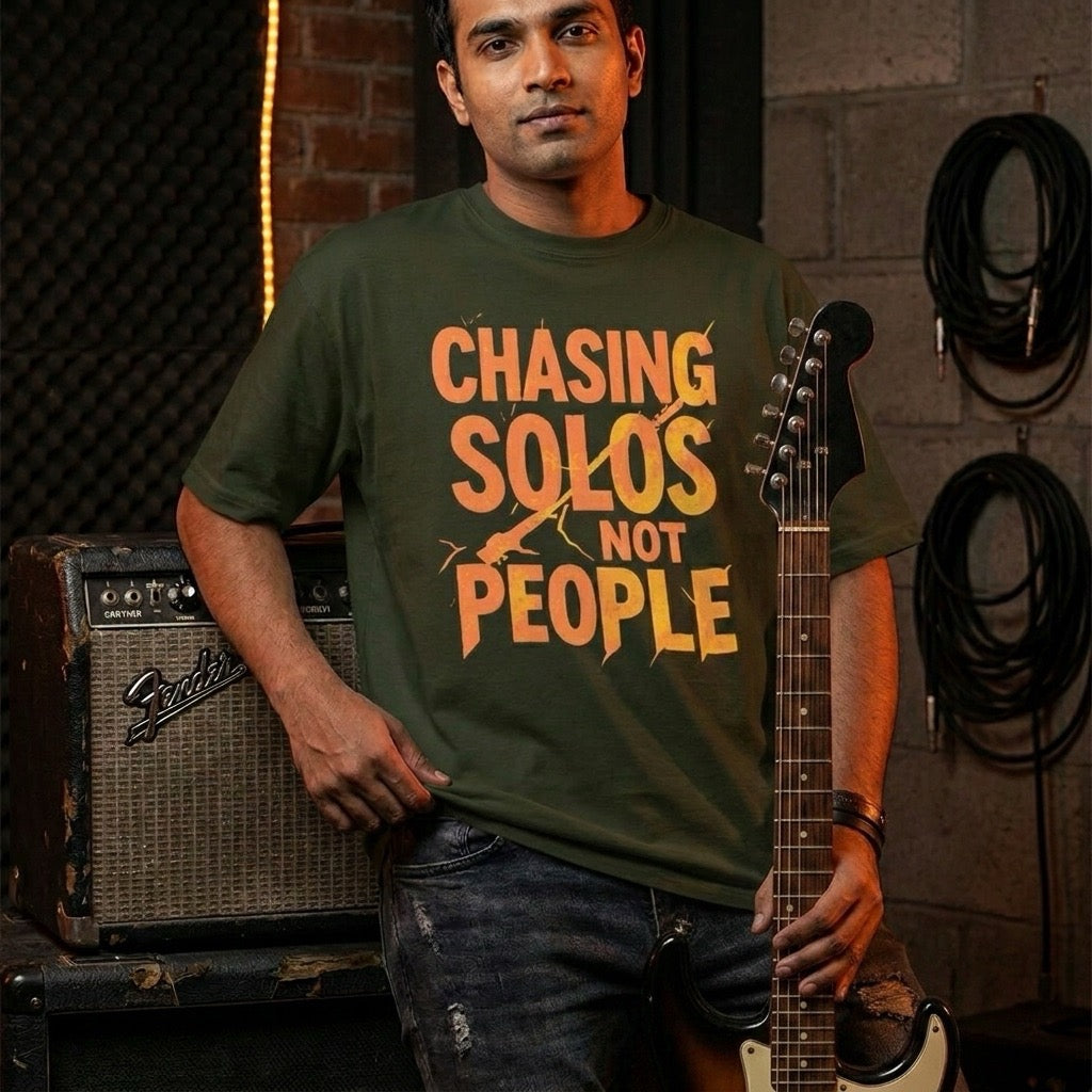 guitarist wearing a green drummerkong t-shirt with 'Chasing Solos Not People' text, holding a guitar in a music studio setting.