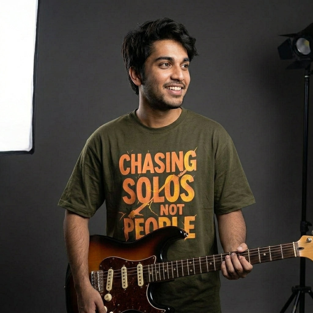Man holding a guitar wearing a Drummerkong t-shirt with text in a studio setting