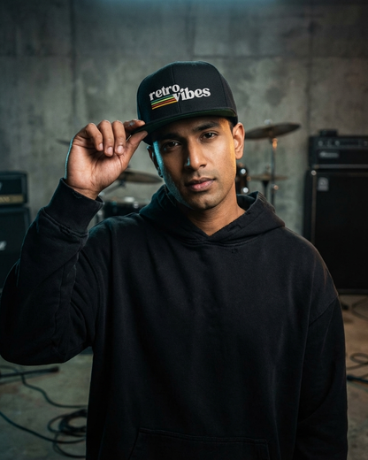 Man wearing a black hoodie and 'retro vibes' snapback cap in a drums and music studio setting